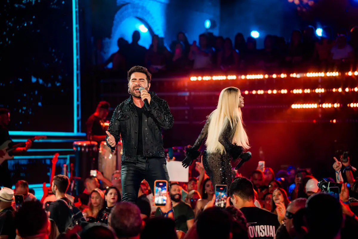Léo Lira canta na beira do palco, com o público de celulares erguidos.