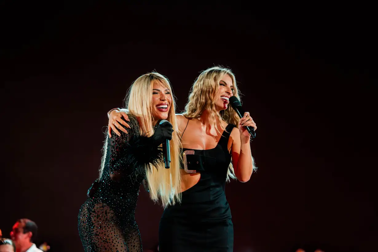 Duas cantoras cantam juntas, abraçadas, no palco.