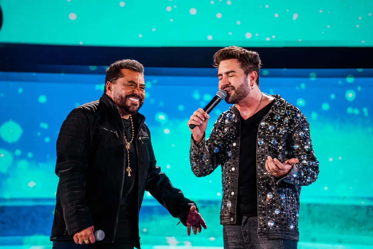 Dois cantores cantam frente a frente, sob luz azul.